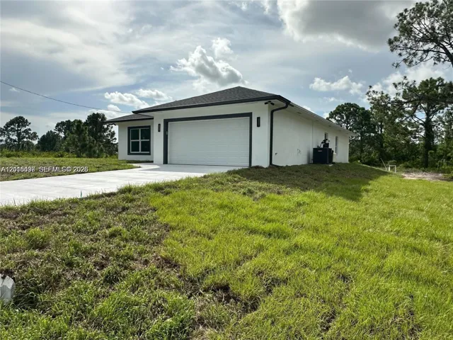 Single-story residence featuring a smooth stucco exterior, dark trim accents, a two-car garage, and a concrete driveway on a grass-covered lot
