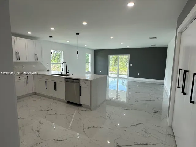 Kitchen featuring white shaker cabinetry, quartz countertops with a waterfall edge, large-format veined tile flooring, recessed lighting, and stainless steel dishwasher