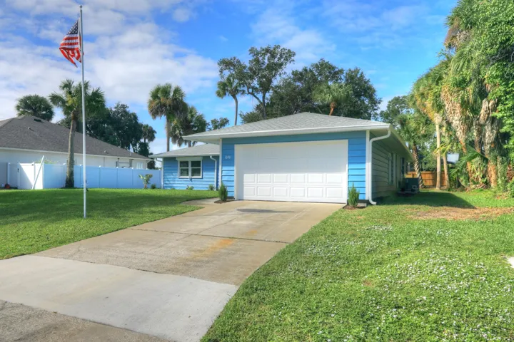 Single-story residence featuring horizontal lap siding, an attached two-car garage, and a concrete driveway, set on a grass-covered lot with mature palm trees
