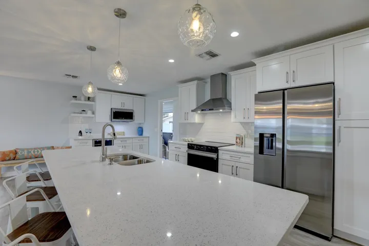 Kitchen featuring a large island with a light-toned solid surface countertop, white shaker-style cabinetry, stainless steel appliances, a stainless steel range hood, and glass pendant lighting