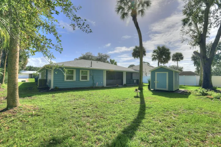 Backyard featuring a grass lawn, detached storage shed, screened-in porch, and mature palm trees