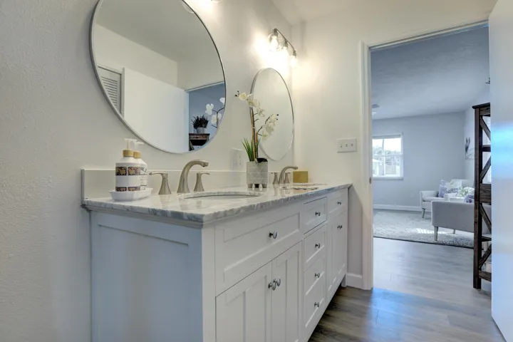 Dual-sink vanity with stone countertop, white shaker-style cabinetry, undermount sinks, and round wall-mounted mirrors