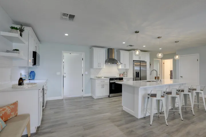 Kitchen featuring a central island with a stone countertop, white shaker-style cabinetry, stainless steel appliances, open shelving, and wood-finish flooring
