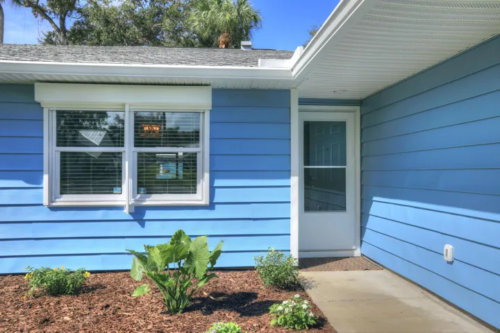 Exterior featuring lap siding, white-framed windows with external storm shutters, and a concrete walkway leading to a glass-panel entry door