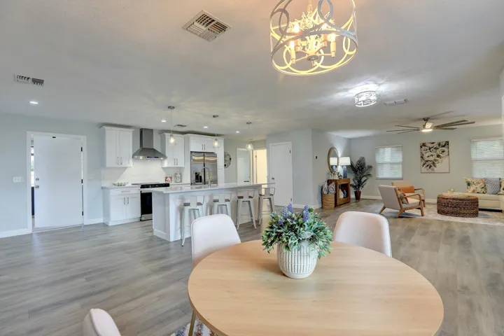 Open-concept interior featuring wood-finish flooring, a kitchen island with stone-finish countertops, shaker-style cabinetry, a stainless steel range hood, and a decorative metallic drum chandelier