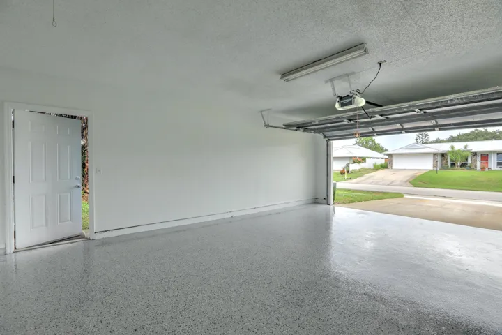 Garage space featuring an epoxy-coated floor, white painted walls, a textured ceiling, a ceiling-mounted light fixture, and a side access door