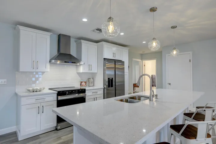 Kitchen featuring white cabinetry, quartz countertops, a stainless steel range hood, subway tile backsplash, and triple glass pendant lighting