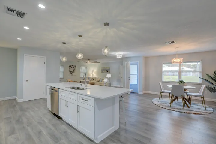 Open-concept space featuring wood-finish flooring, a kitchen island with quartz countertops, stainless steel dishwasher, and spherical pendant lighting