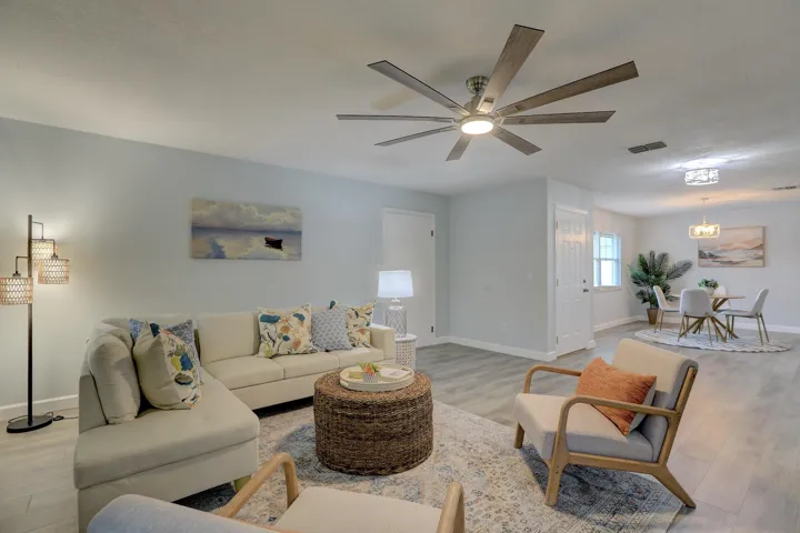 Open living area featuring wood-finish flooring, a multi-blade ceiling fan with integrated lighting, and a neutral color palette