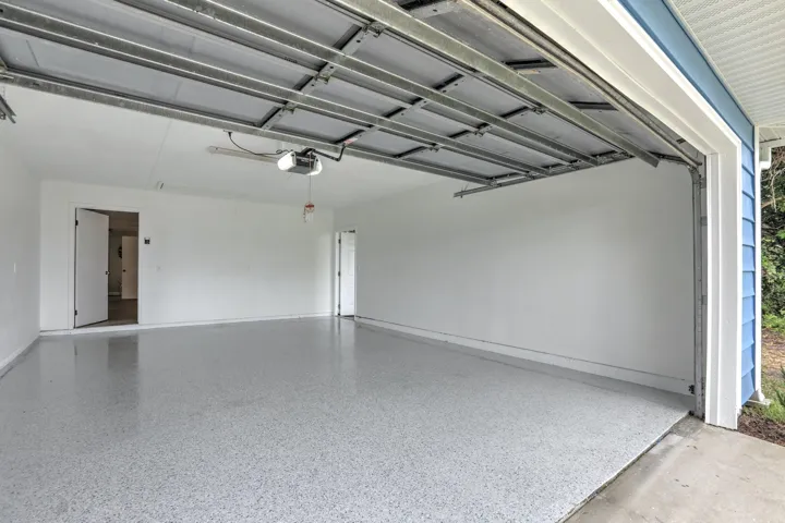 Attached two-car garage featuring epoxy-finished concrete flooring, finished drywall, an overhead automatic door opener, and interior access doors