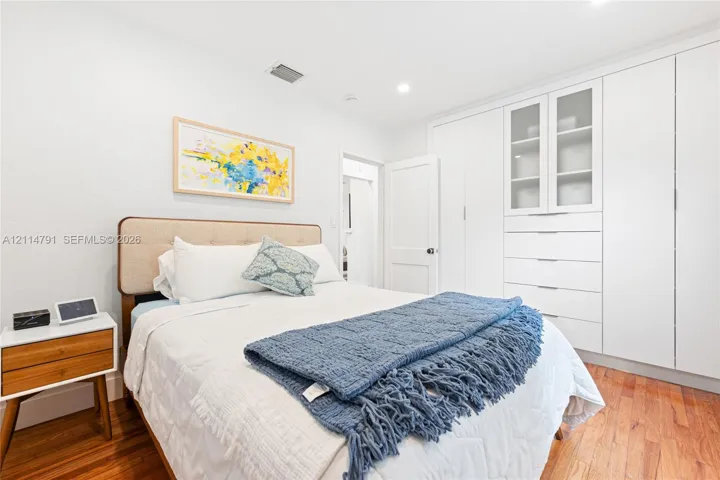 Room featuring wood-finish flooring, recessed lighting, and expansive floor-to-ceiling built-in cabinetry with integrated drawers and glass-front upper shelving