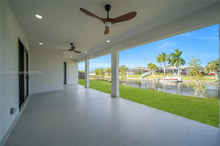Covered lanai featuring large-format tile flooring, recessed lighting, and dual ceiling fans, opening to a grass-covered backyard with direct water frontage