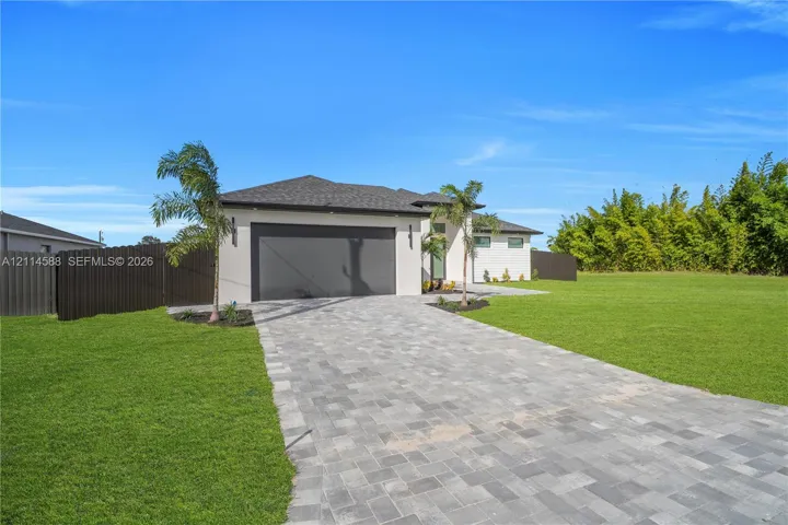 Single-story exterior featuring a paver driveway, two-car garage, manicured lawn, and perimeter privacy fencing