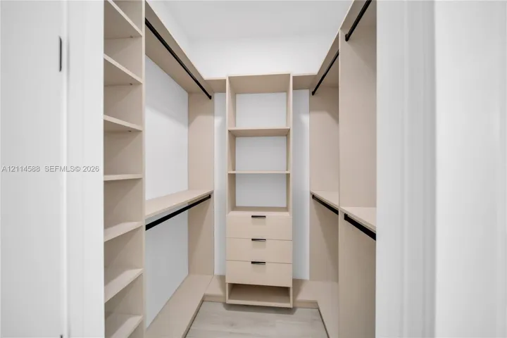 Custom walk-in closet featuring light-toned built-in cabinetry, integrated shelving, three storage drawers with matte black hardware, and wood-finish flooring