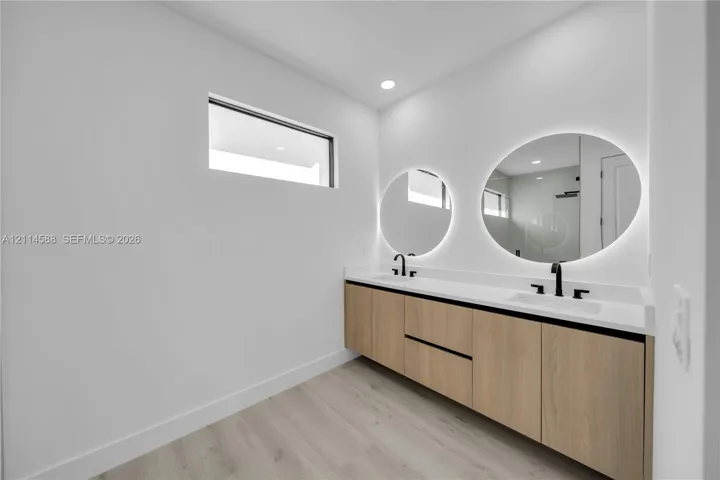 Floating dual-sink vanity featuring wood-finish cabinetry, solid-surface countertops, matte black fixtures, and circular backlit mirrors
