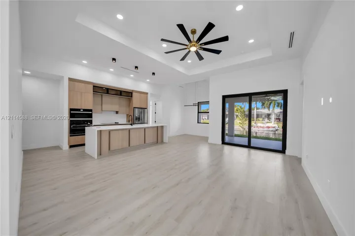 Open-concept living space featuring wood-finish flooring, recessed lighting, a coffered ceiling with a multi-blade ceiling fan, and sliding glass doors