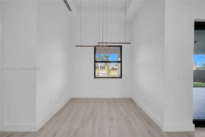 High-ceiling interior featuring wood-finish flooring, a single-pane window with a black frame, and a modern linear pendant light fixture