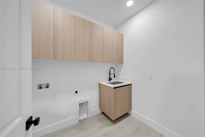 Laundry area featuring wood-finish cabinetry, a white countertop with an integrated sink, matte black faucet hardware, and wood-finish flooring