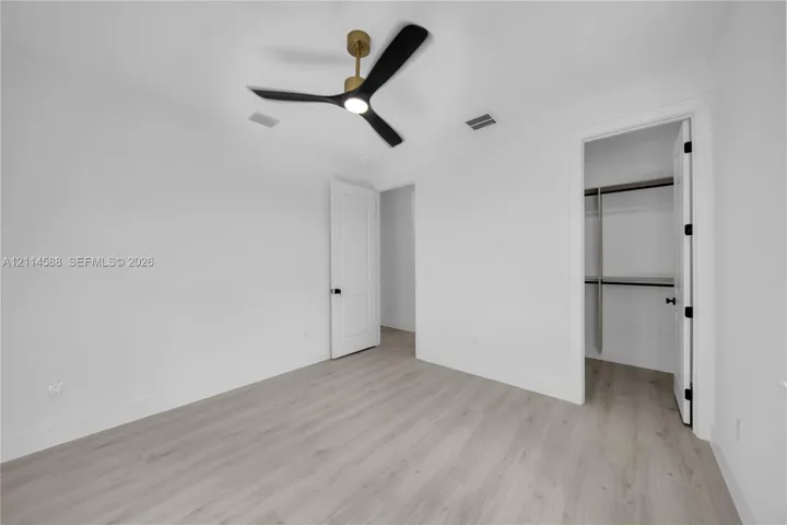 Neutral interior featuring light-toned wood-finish flooring, a modern three-blade ceiling fan with integrated lighting, solid-core interior doors, and a built-in closet system