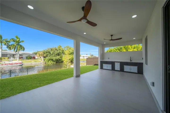 Covered patio featuring large-format tile flooring, recessed lighting, dual ceiling fans, and a built-in outdoor kitchen with sink and cabinetry