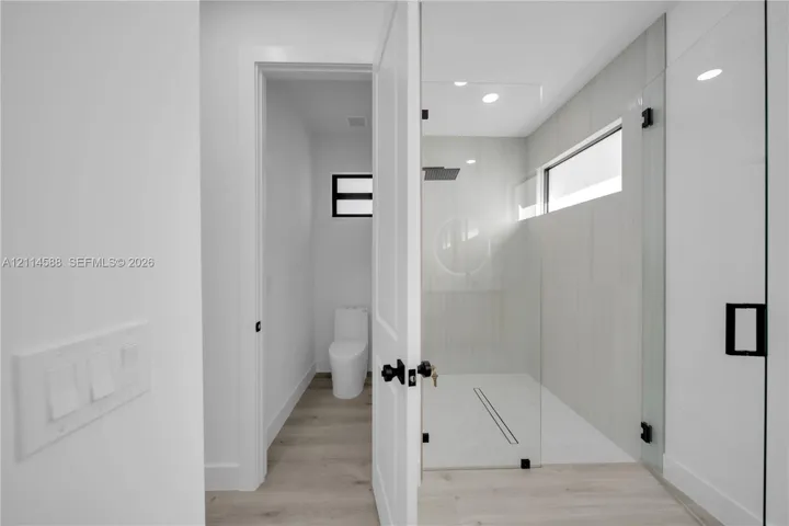 Walk-in glass-enclosed shower featuring floor-to-ceiling tile, linear drain, and rainfall showerhead, paired with wood-finish flooring and matte black hardware throughout