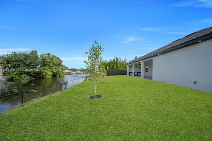 Waterfront backyard featuring a manicured lawn, covered patio, outdoor kitchen, and metal mesh perimeter fencing