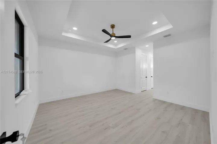 Room featuring a recessed tray ceiling, wood-finish flooring, recessed lighting, and a three-blade ceiling fan with a metallic finish