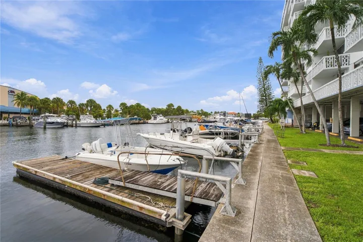 Waterfront property featuring a private boat slip, concrete bulkhead, manicured lawn, and mature palm trees