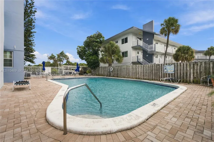 Inground swimming pool with a metal handrail, surrounded by a paved brick deck and enclosed by a perimeter fence