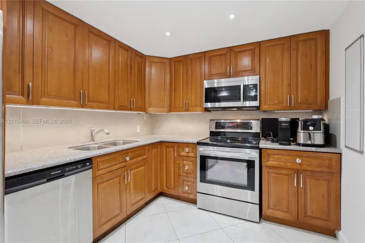Kitchen featuring wood cabinetry, stone-finish countertops, stainless steel appliances, recessed ceiling lighting, and tile flooring