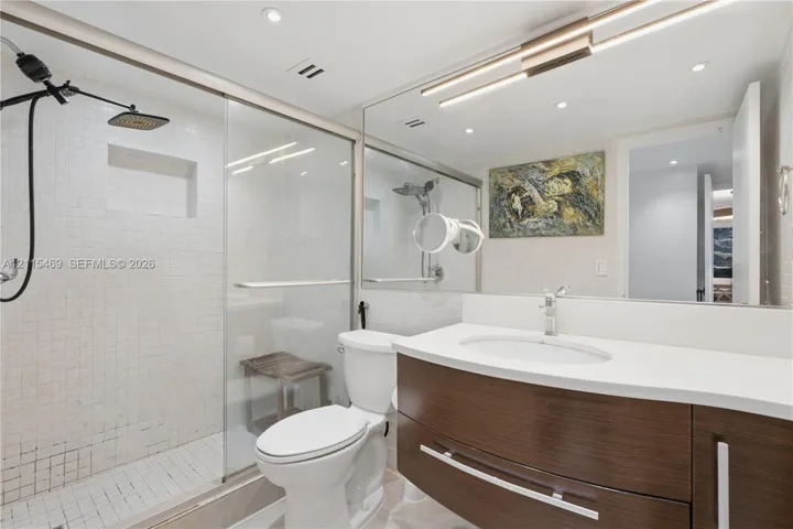 Floating vanity with a stone countertop, under-mount sink, matte black rain-style shower head, built-in recessed shower niche, and glass-enclosed shower with wall-mounted fixtures