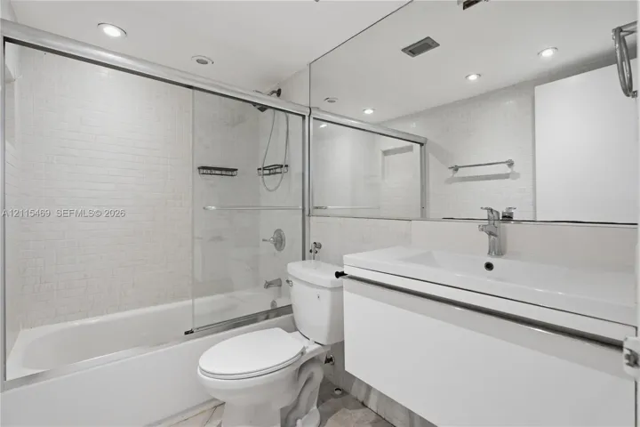 Bathroom featuring a floating vanity with an integrated sink, a glass-enclosed shower-tub combination with mosaic tile surround, and a wall-to-wall mirror