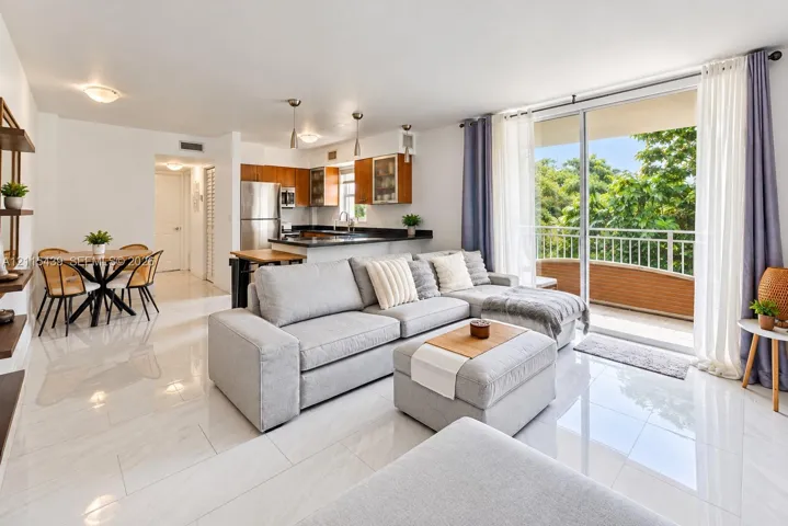 Open-concept living space featuring high-gloss tile flooring, stainless steel kitchen appliances, wood-tone cabinetry, recessed lighting, and sliding glass doors with direct exterior access to a railed balcony