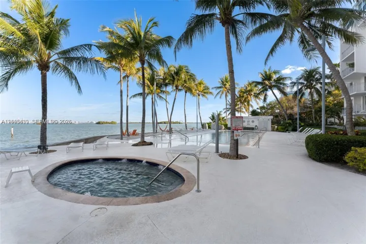 Waterfront pool deck featuring an in-ground spa, stone-finished coping, and mature palm trees