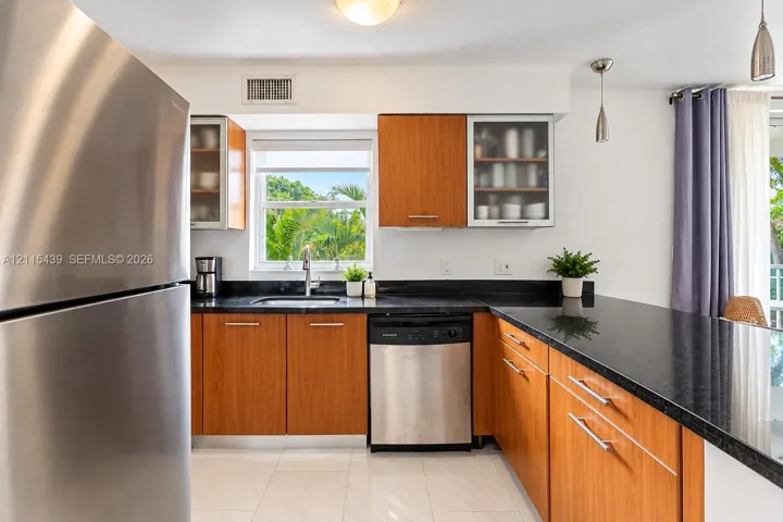 Kitchen featuring wood-finish cabinetry, dark stone-style countertops, stainless steel appliances, and large-format tile flooring