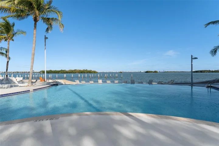 Infinity-edge swimming pool featuring a tiled perimeter, expansive concrete decking, and direct water frontage