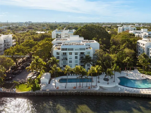 Waterfront multi-story residential building featuring two swimming pools, paved sun decks, mature palm trees, and a reinforced bulkhead