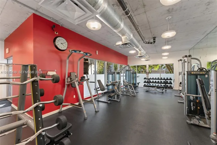 Fitness facility featuring exposed concrete ceilings, industrial ductwork, rubberized flooring, pendant lighting, and floor-to-ceiling windows