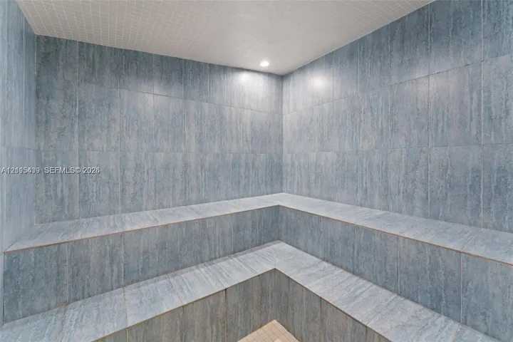 Steam room featuring floor-to-ceiling blue tile, multi-level built-in bench seating, and recessed ceiling lighting