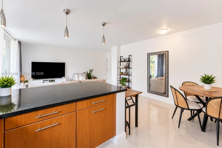 Kitchen featuring a stone-topped island with wood-veneer cabinetry, polished tile flooring, and metallic pendant lighting