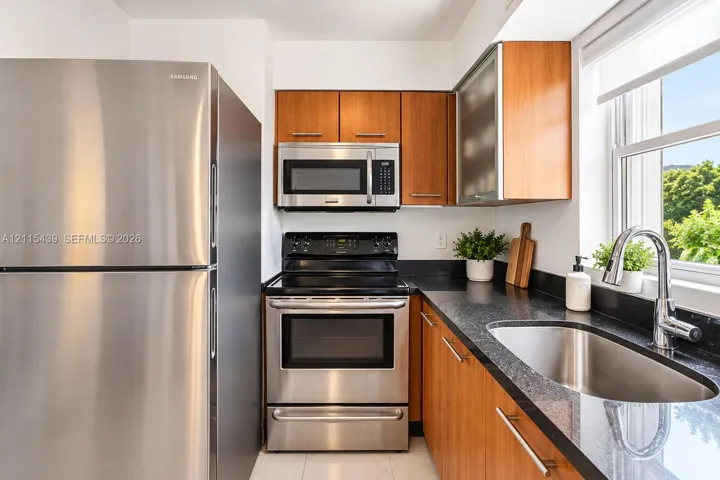 Kitchen featuring stainless steel appliances, dark stone countertops, natural wood-finish cabinetry, an undermount sink with a gooseneck faucet, and an integrated microwave