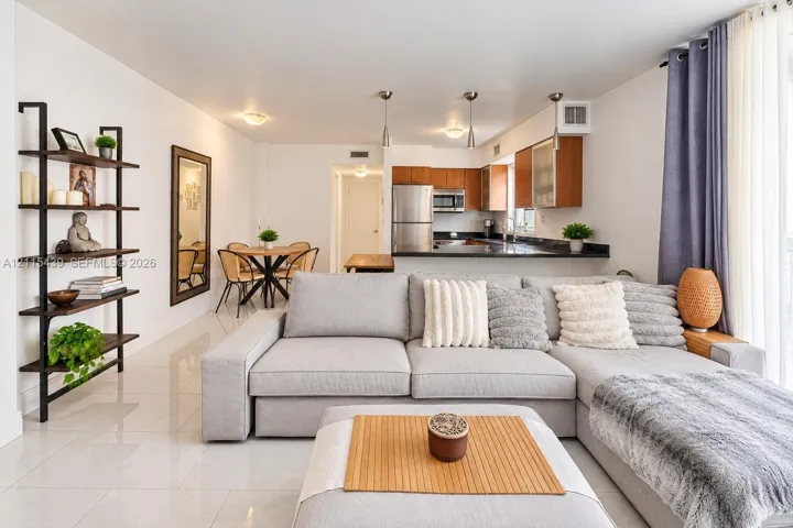 Open-concept living space featuring ceramic tile flooring, kitchen with stainless steel appliances, dark stone-finish countertops, and built-in wood cabinetry