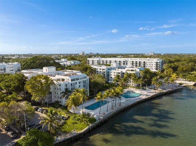 Waterfront multi-story residential buildings featuring dual swimming pools, paved sun decks, and mature palm landscaping along the shoreline