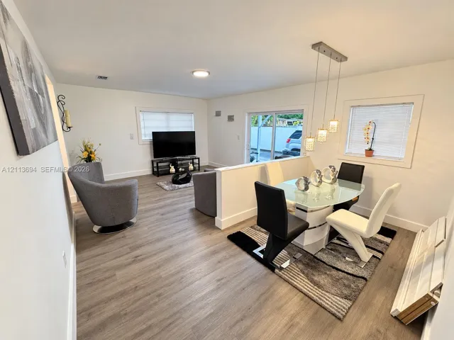 Open-concept interior featuring wood-finish flooring, a half-wall partition, modern multi-pendant lighting, and sliding glass doors
