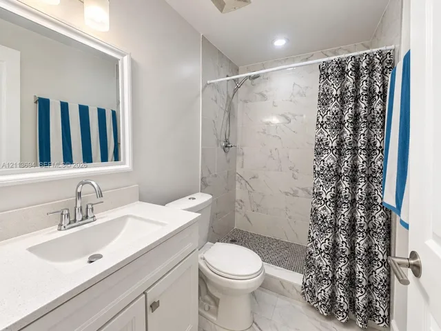 Bathroom featuring a vanity with a composite countertop and integrated basin, large-format tile shower surround, mosaic pebble-style flooring, and chrome hardware