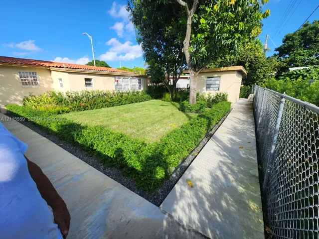 Backyard featuring a manicured lawn, perimeter hedge landscaping, concrete walkways, a mature tree, and a chain-link fence