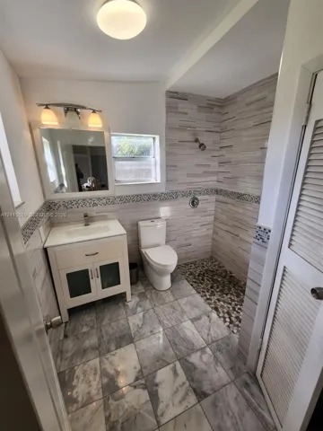 Bathroom featuring stone-tile flooring, vanity with inset basin, walk-in shower with pebble-stone flooring, decorative tile inlay, and wall-mounted light fixtures