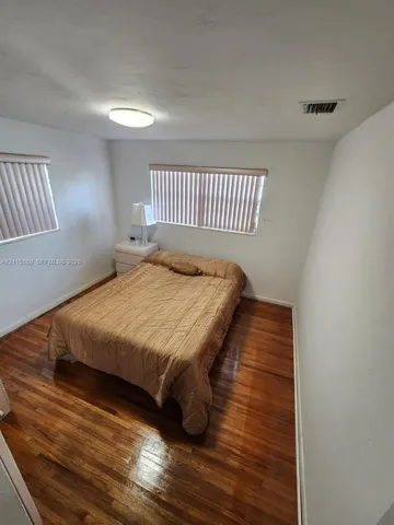 Room with wood-finish flooring, two windows with vertical blinds, and a flush-mount ceiling light fixture