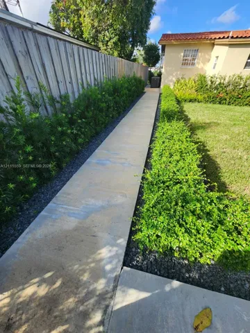 Concrete pathway flanked by manicured privacy hedges and gravel bordering, complemented by a fenced perimeter