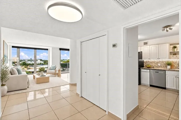 Neutral-toned tile flooring, floor-to-ceiling windows, built-in dual-door closet, and kitchen featuring white cabinetry with stainless steel appliances